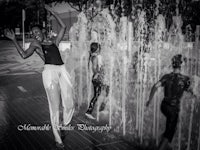 a black and white photo of a woman dancing in front of a fountain