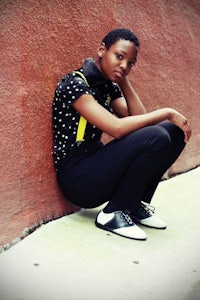 a young woman crouching down next to a wall